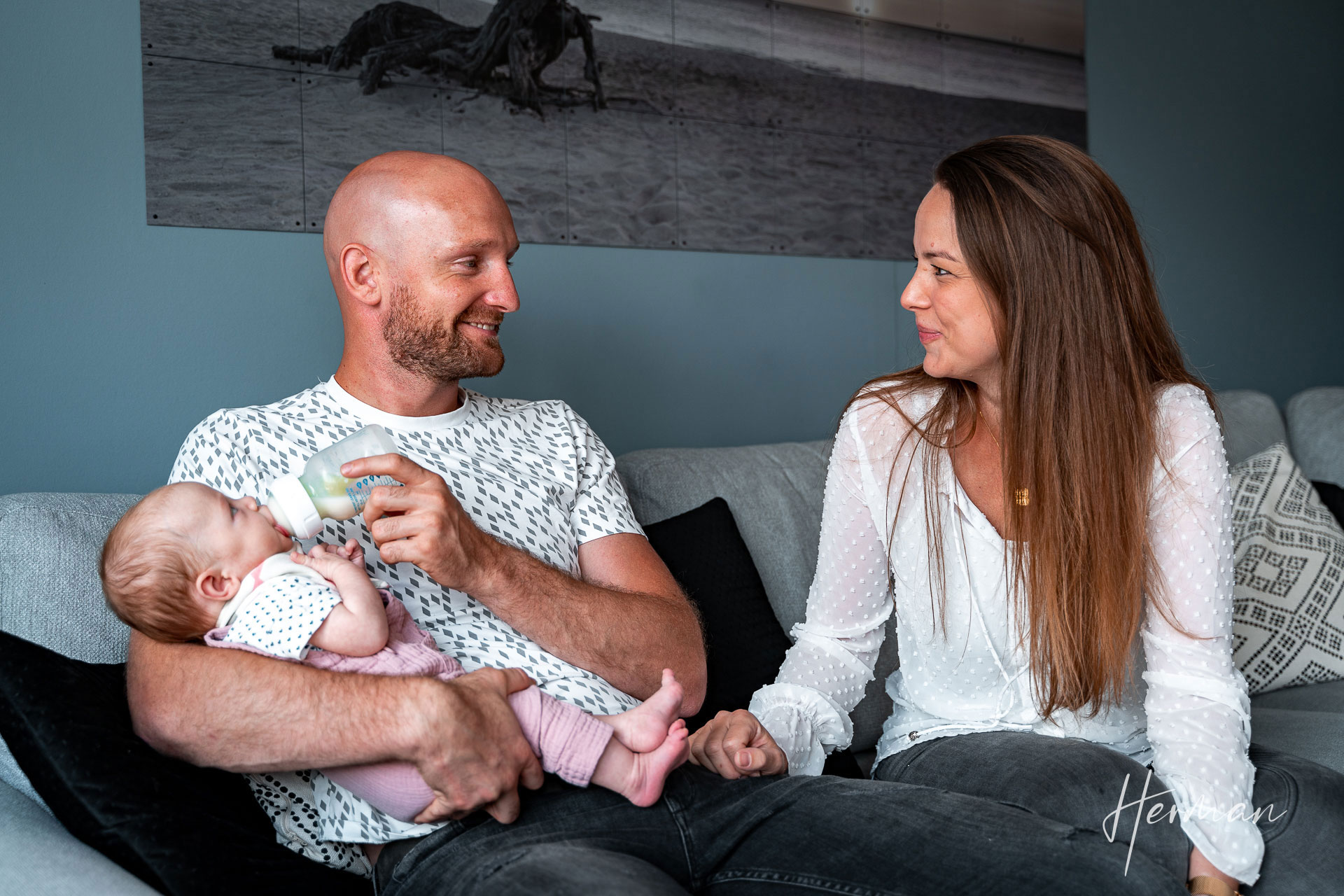 Lifestyle fotoshoot - Stel lacht verliefd naar elkaar en kind krijgt de fles - Herman Fotografie